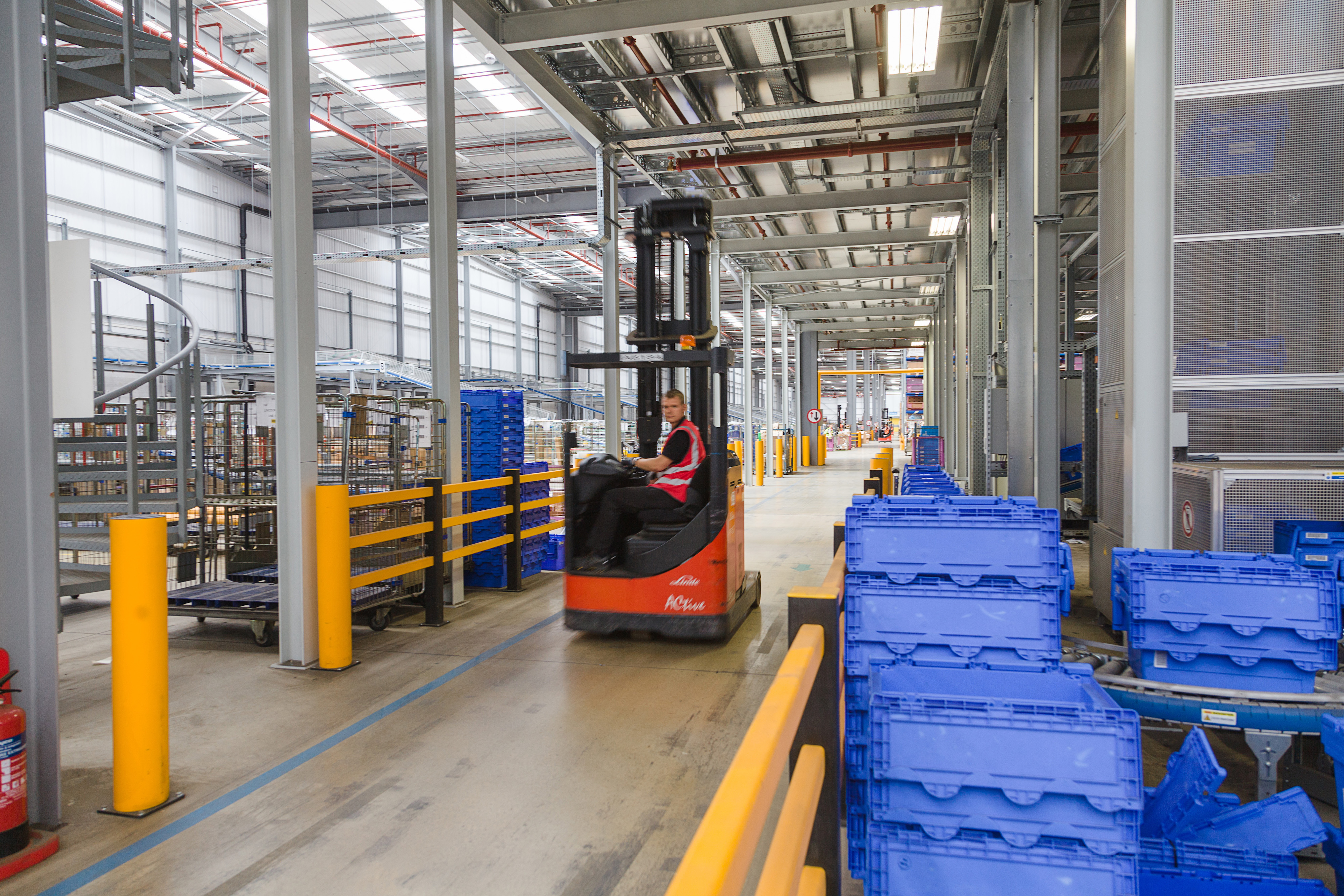 Interior photo of Prologis North Hampton Pineham DC1, showing spiral meatal stairs on the left, blue boxes and yellow bumper guards, and a person driving a red forklift