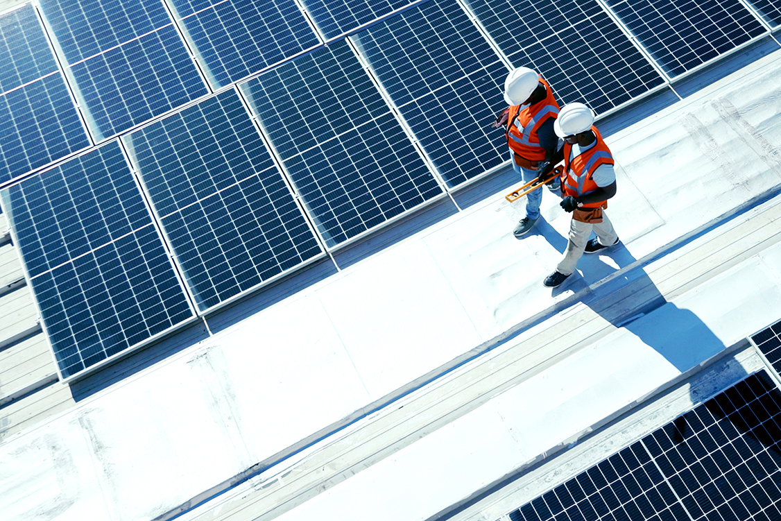 Two workers walking on a roof with solar panels