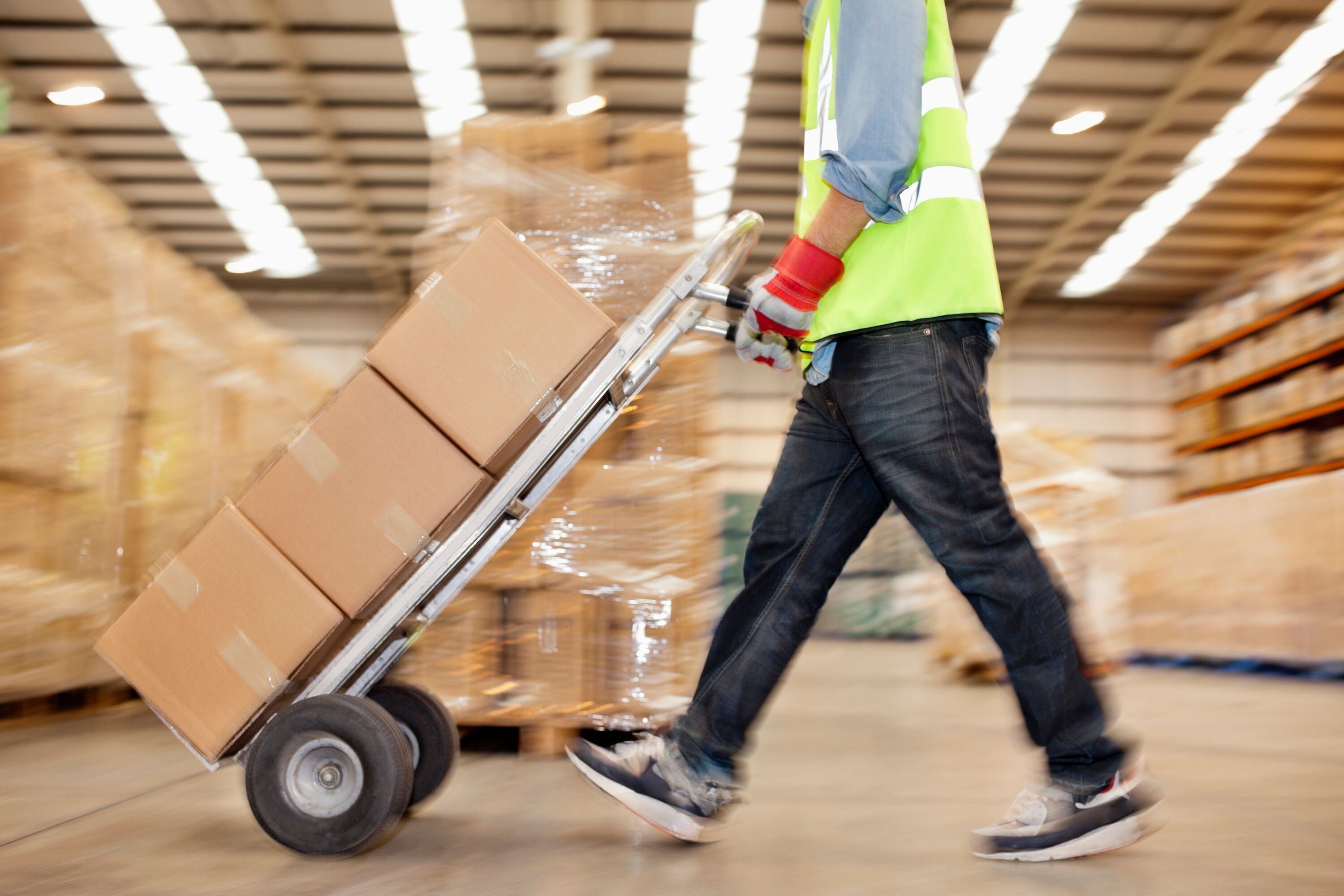 Warehouse worker pushing boxes with a hand truck.