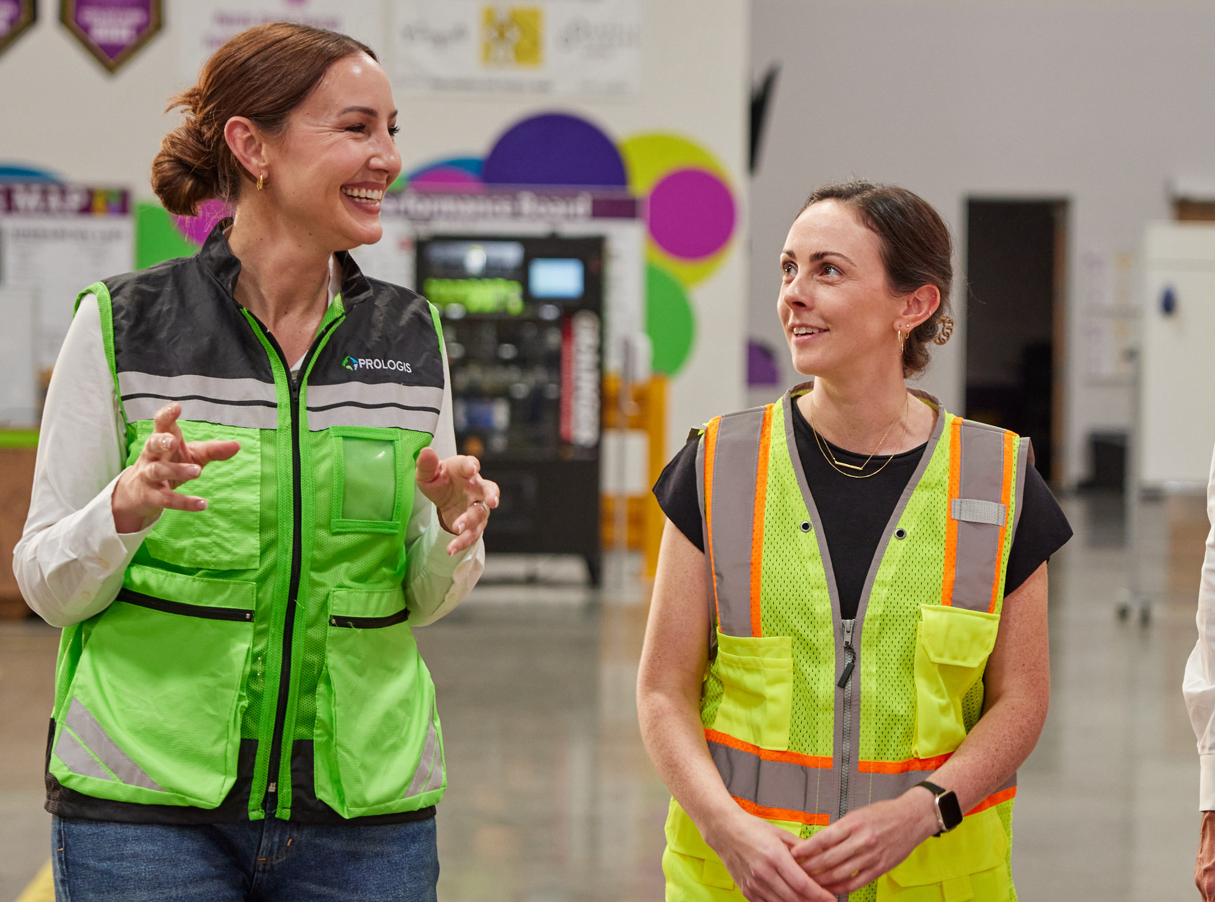 Two women in safety vests talking in a warehouse