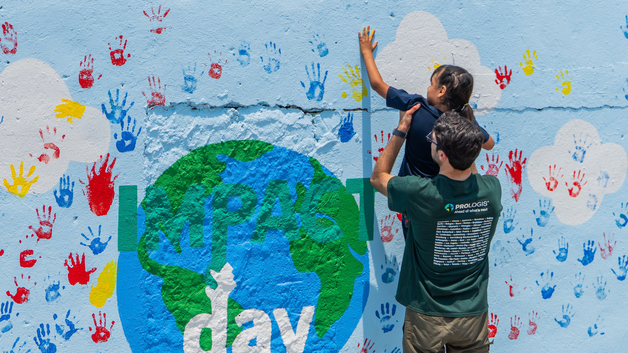 A man holding a child up to a mural to place a handprint