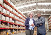 A man and a woman in a warehouse with racks of pallets in the background