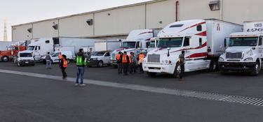 A photo of workers in orange and green vests standing outside in a full truck court at Prologis Tres Rios