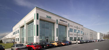 An exterior photo of Prologis Park 275 with cars parked outside, and an amazon.com logo displayed on the front of the building