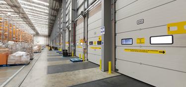 A photo of the interior dock doors at Prolgois RFI DIRFT Sainsbury. The dock doors have yellow safety signage on them, and in the background there is tall orange racking.