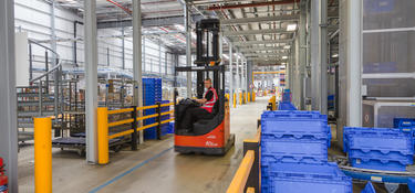 Interior photo of Prologis North Hampton Pineham DC1, showing spiral meatal stairs on the left, blue boxes and yellow bumper guards, and a person driving a red forklift