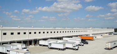 Exterior warehouse shot of Prologis Park Beacon Lakes 13 in Miami, Florida loading dock with white semi trucks driving in and out and orange truck parked