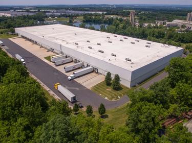An exterior aerial shot of Prologis Lehigh Valley East surrounded by lush green trees with trucks parked in the truck court