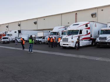 A photo of workers in orange and green vests standing outside in a full truck court at Prologis Tres Rios