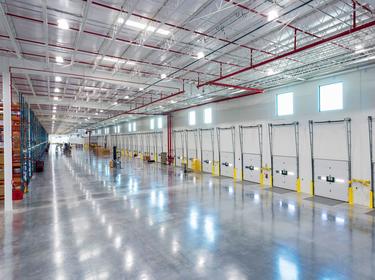 A photo of the inside of Prologis Apodaca  6. A wall covered in dockdoors is on the right of the image, and blue and orange racking, numbered by aisle is on the left.