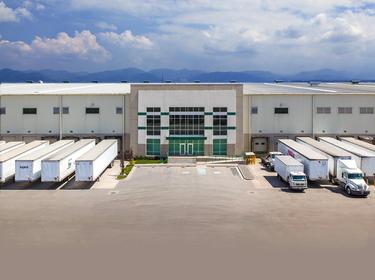 A photo of the main entrance and truck courts at Prologis Toluca 4. The truck court is full of white semi-truck trailers and mountains with clouds above are in the background