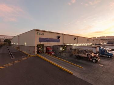 A photo of the truck courts at Prologis Agave LC 2 at dusk. The truck court is full of trucks being loaded through dock doors and two other warehouses are in the background