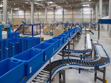 A photo of a blue conveyor racking system and blue bins inside of Prologis Isle Dabeau DC20. In the background there is standard racking stacked with product.