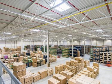 A photo of the inside of Prologis Munich East DC1. In the foreground there are cardboard boxes tacked on pallets and in the background there are boxes stacked on blue and green racking.