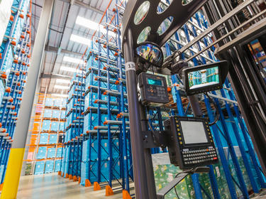 An interior photo of a warehouse showing a picking vehicle with scanners, and blue and orange racking in the background