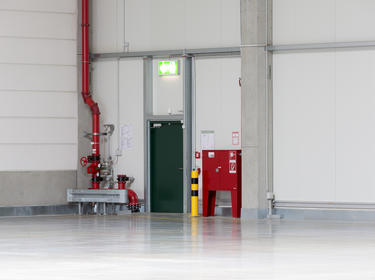 A photo of a green exit door to a warehouse, with a large red pipe to the left of the door