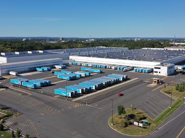 An aerial photo of Prologis ports carteret showing solar panels on the roof, and white and blue Amazon trucks in the truck courts