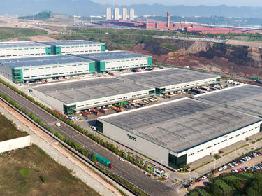 Angled aerial shot of Prologis Chongqing Liangjiang Logistics Center in China with industrial park in the distance, surrounding green space and trucks parked in loading area