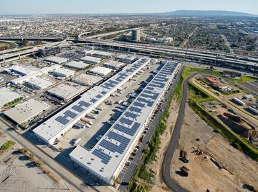 Angled aerial shot of LAX Logistics Center in Los Angeles, California with solar panels on the roof, surrounded by construction, busy highways and city scape