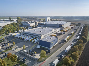 Aerial view of Dachser branded warehouse building and semi trucks at Prologis Munich Neufahrn Distribution Center 1 in Germany surrounded fields and trees
