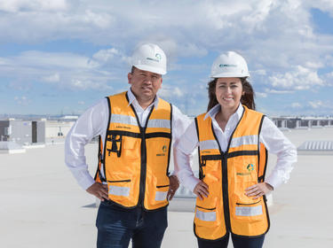 Prologis Employees Adrian Olmeda and Mayra Coronado wearing Prologis hard hats and orange vests standing on the roof of Prologis Park Centro Industrial Juarez in Juarez, Mexico