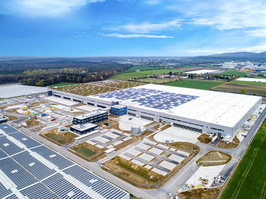 Aerial angled view of build-to-suit distribution center Prologis Park Muggensturm in Muggensturm, Germany with green landscaped and solar panels installed on roof, surrounded by green fields and trees