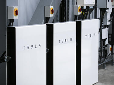 Three large TESLA batteries mounted on a wall inside a warehouse