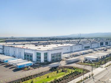 Exterior shot of Prologis International Park of Commerce in Tracy, California with semi trailers parked in loading docks, semi trucks driving in and out and windmills in the distance