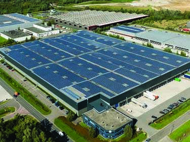 Exterior shot of a warehouse with rooftop solar panels and surrounded by a green landscape
