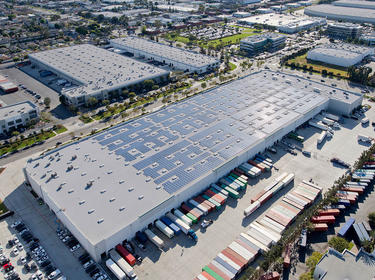 Aerial shot of the buildings at Prologis Capelin Distribution Center, with solar panels on the roof and trucks, shipping containers and cars parked outside.