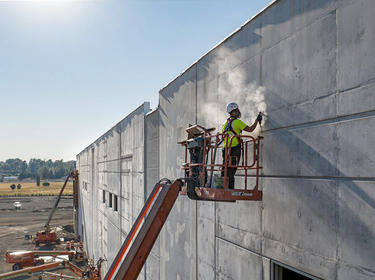 A construction workers sands down an outer wall at a new build site