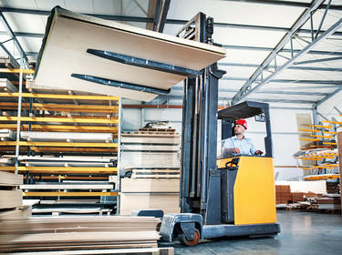 Forklift operator storing some plywood panels at wood working factory