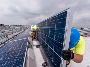 2 employees install solar panel on rooftop