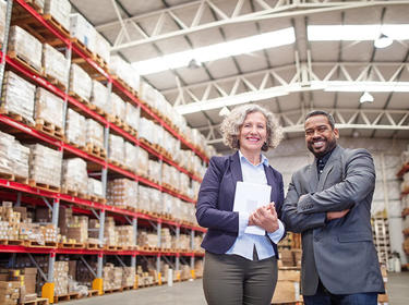 A man and a woman in a warehouse with racks of pallets in the background