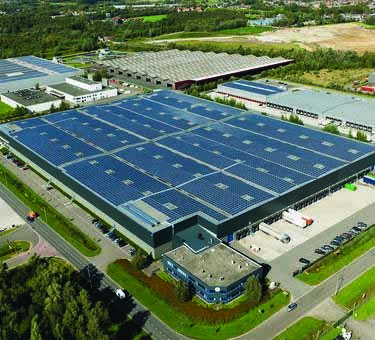 Exterior shot of a warehouse with rooftop solar panels and surrounded by a green landscape