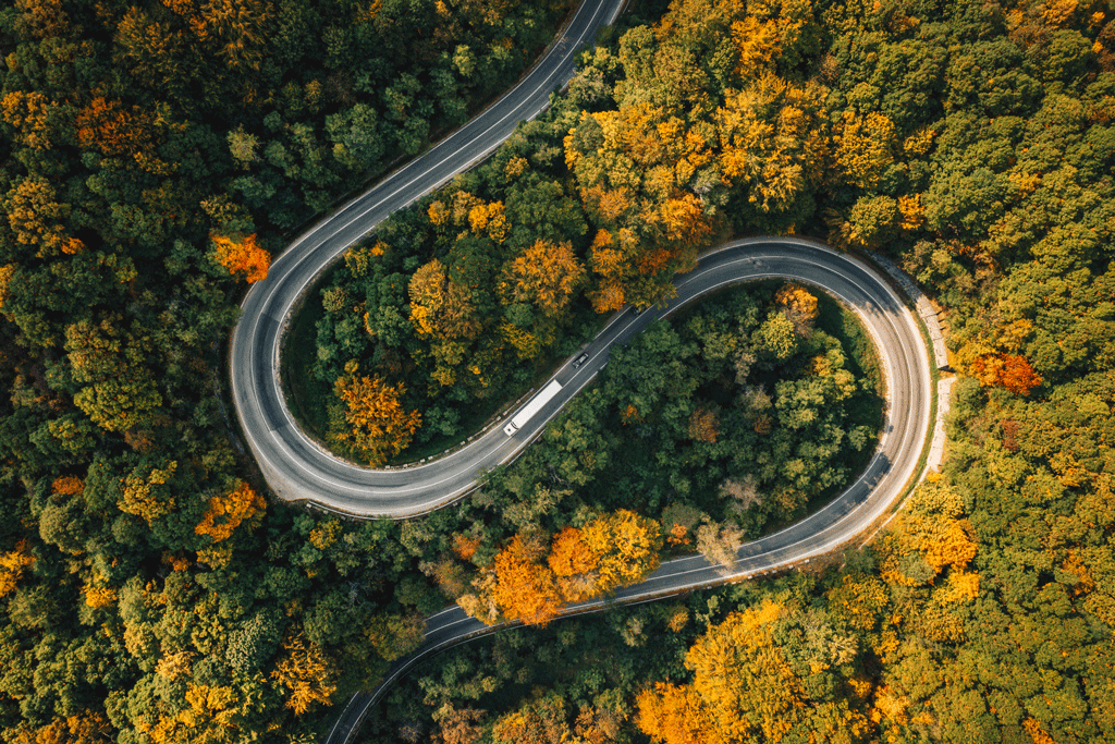 71f7737cc171a1fd5f2b640886829573.png An electric truck driving on a winding road through fall trees