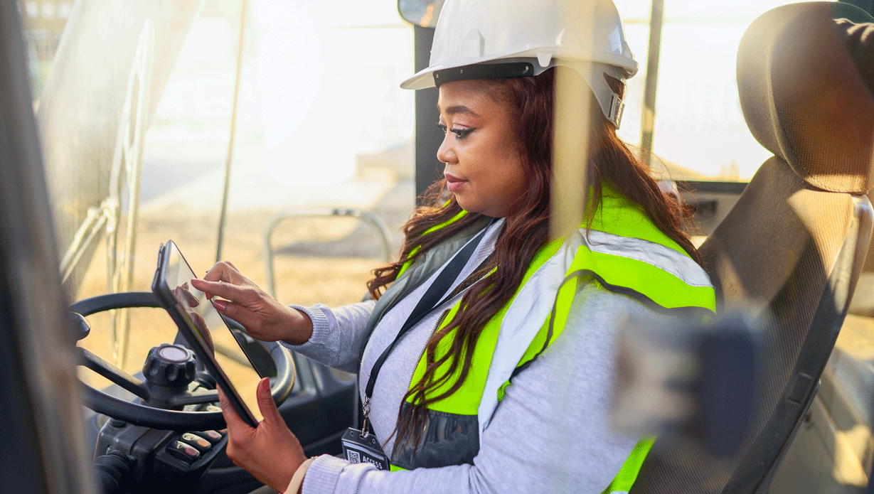 8edaea850cdec975351289f49c55150e.png Woman driving a forklift in a white hard hat and safety vest