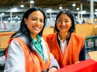 Two women smiling in a warehouse in orange vests Two women smiling in a warehouse in orange vests